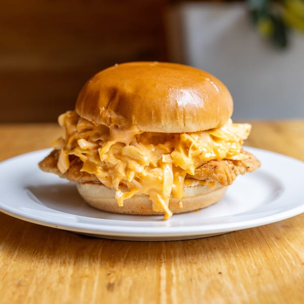 Golden fried chicken sandwich topped with creamy orange coleslaw on a white plate.