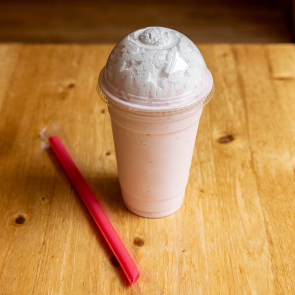 Pink milkshake with whipped cream and a red straw on a wooden table.