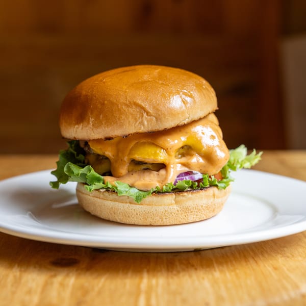 Cheeseburger with melted cheese, special sauce, lettuce, and red onion on a white plate.