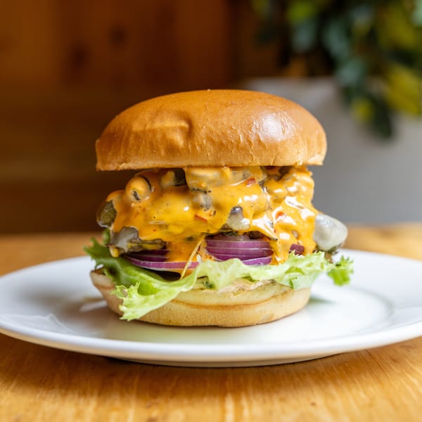 Gourmet burger with gooey cheese sauce, pickles, red onion, and fresh lettuce on a brioche bun.