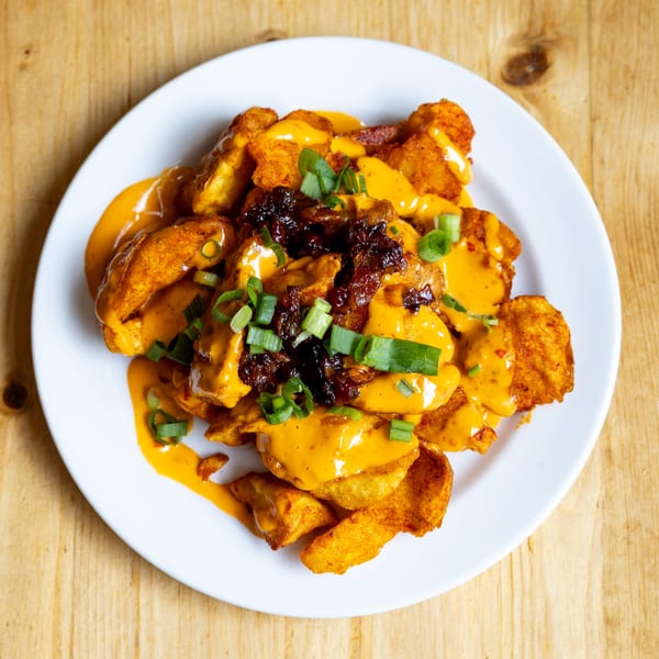 Crispy potato wedges topped with melted cheese, bacon bits, and chopped green onions on a white plate.