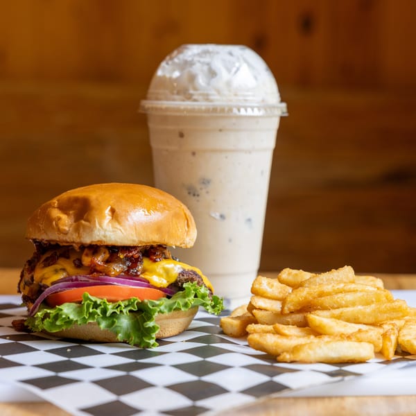 A cheeseburger with lettuce, tomato, onion, and bacon, with fries and a milkshake.