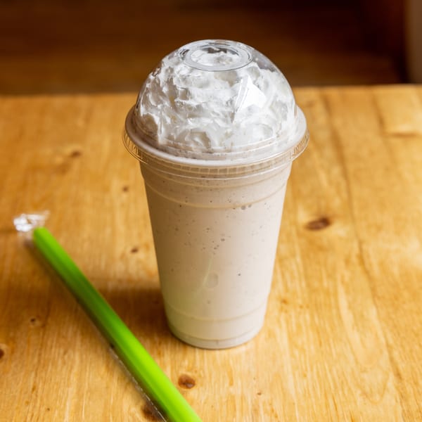 A vanilla milkshake with whipped cream and a green straw on a wooden table.