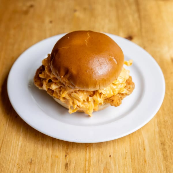 A fried chicken sandwich topped with macaroni and cheese on a white plate.